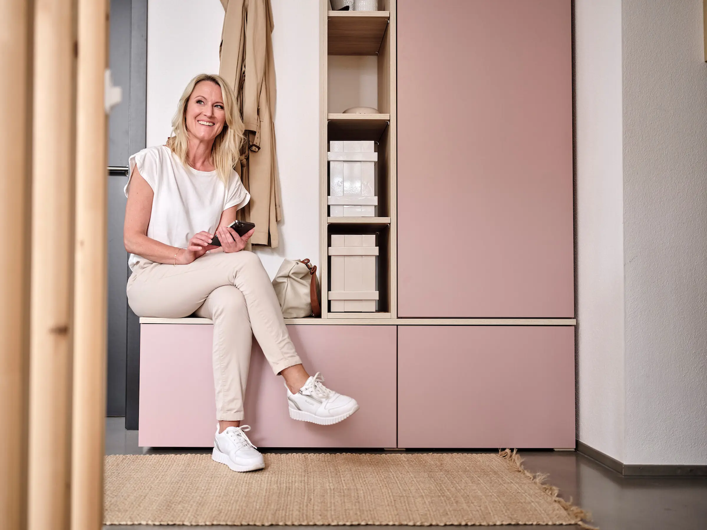 Blonde Frau sitzt auf rosafarbener Garderobe