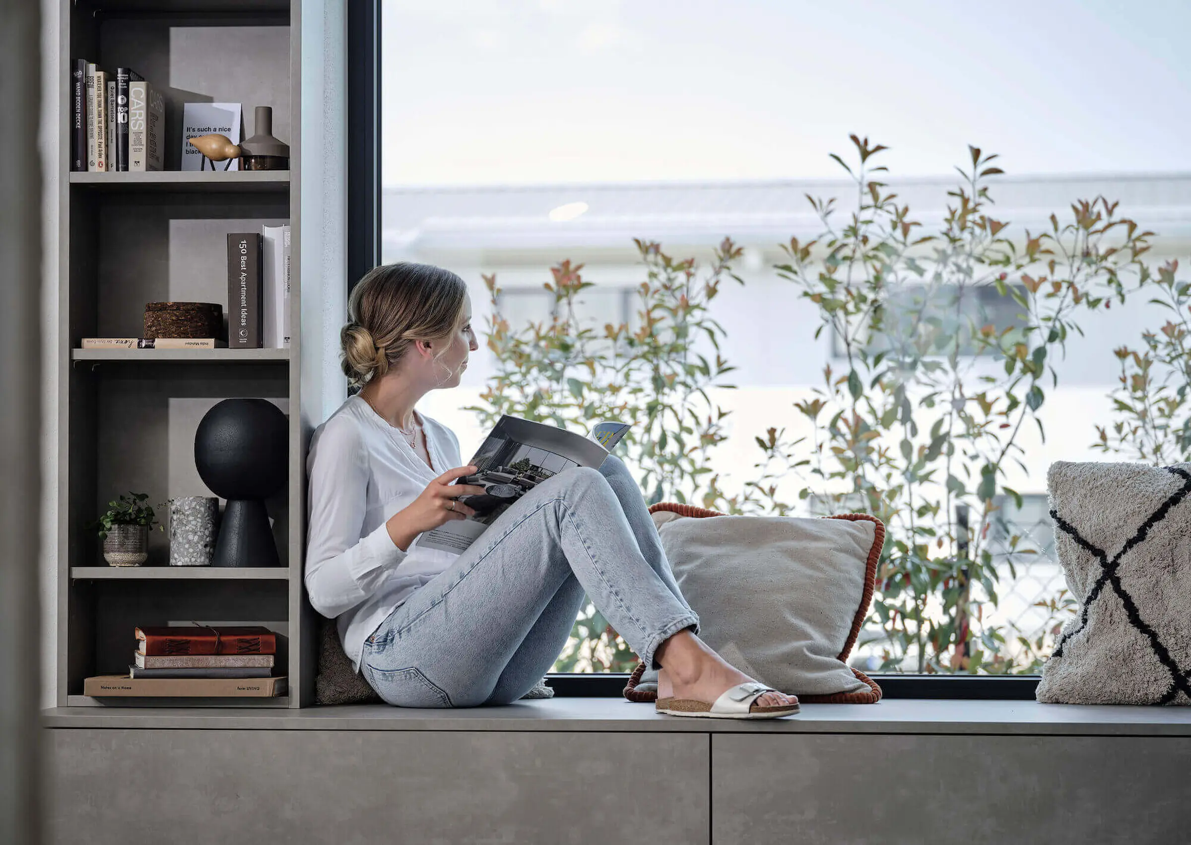 Frau Sitz auf Sideboard liest ein Buch und schaut aus dem Fenster.