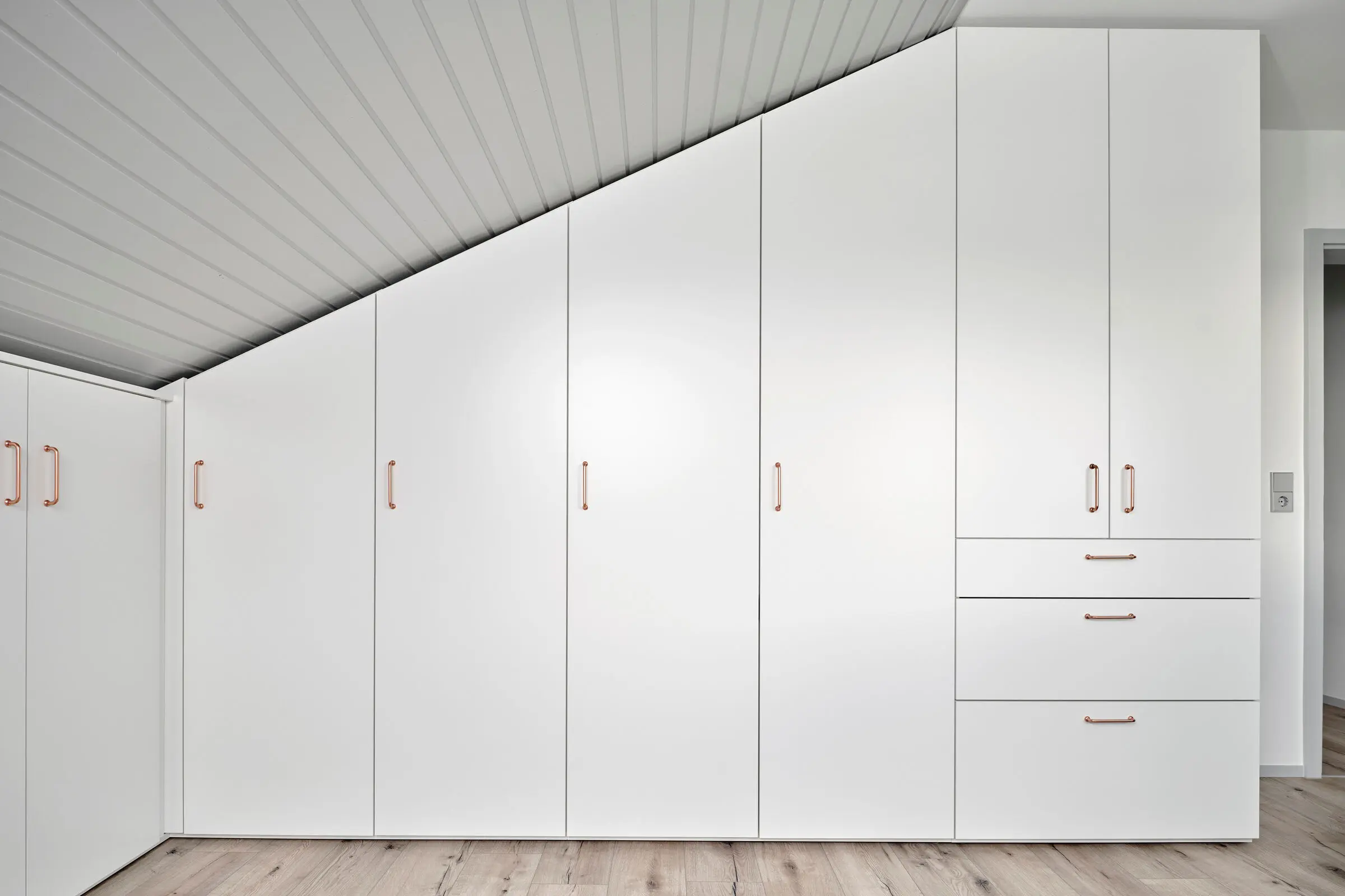 Weisser Dachschrägenschrank mit Griffen.