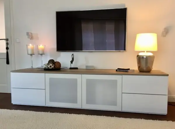 Weisses Sideboard mit Akustikstoff in Weiss, mit Dekoration und TV.