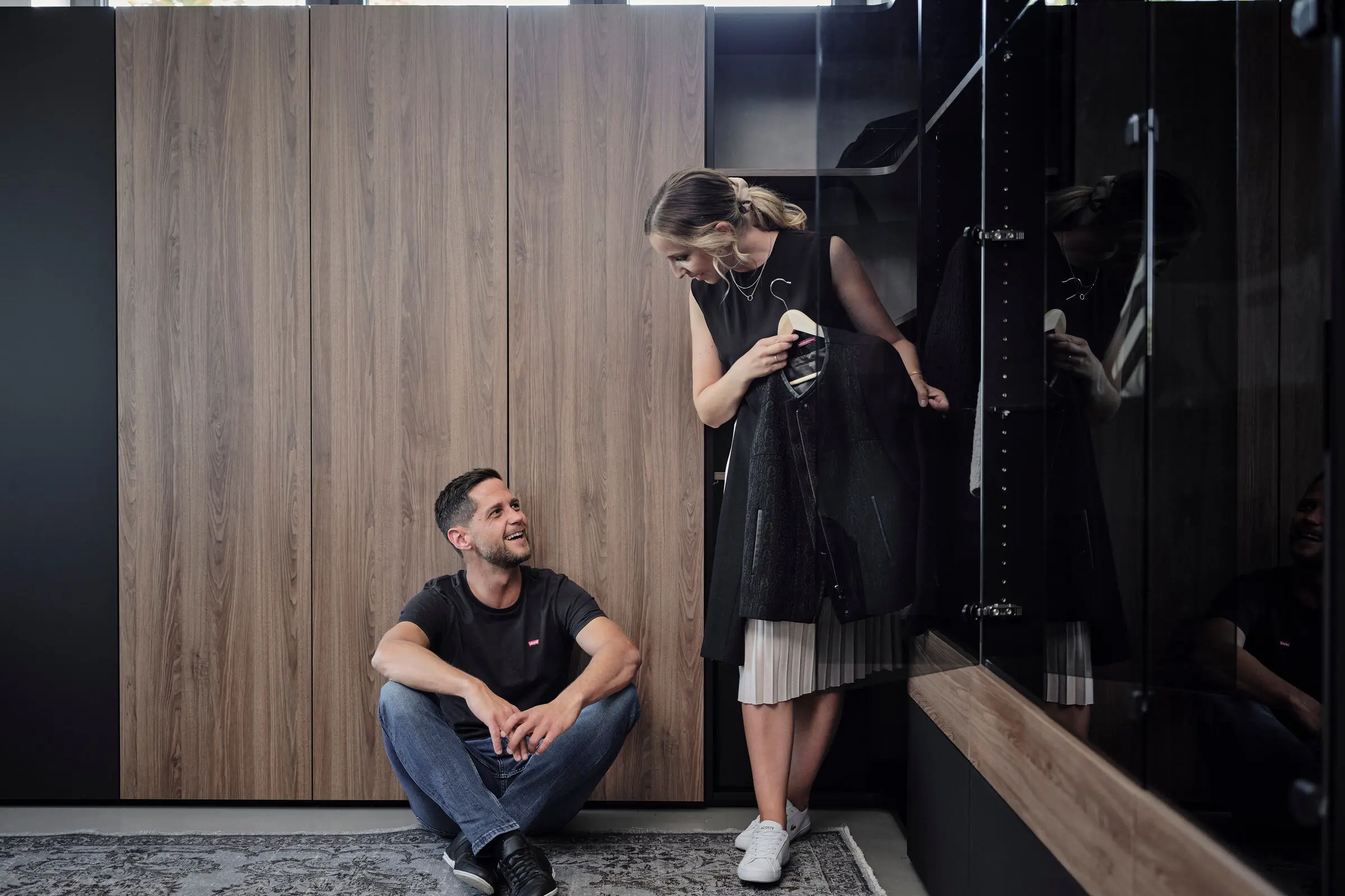 Mann und Frau vor Schrank in Schwarz mit Fronten aus Holz.