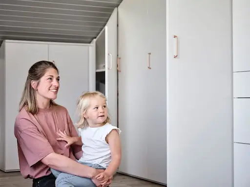 Frau und Kind neben weißen Kleiderschrank.