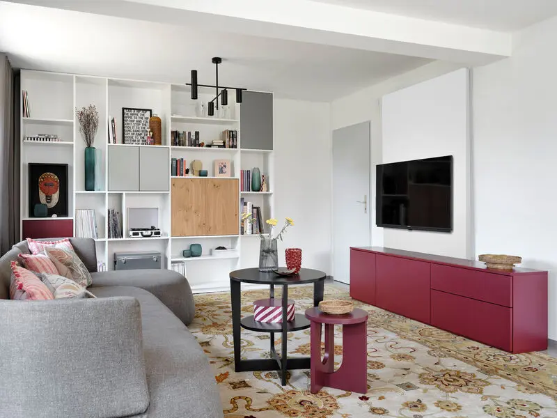 Rotes Sideboard im bunten Wohnzimmer und Wohnwand im Hintergrund.